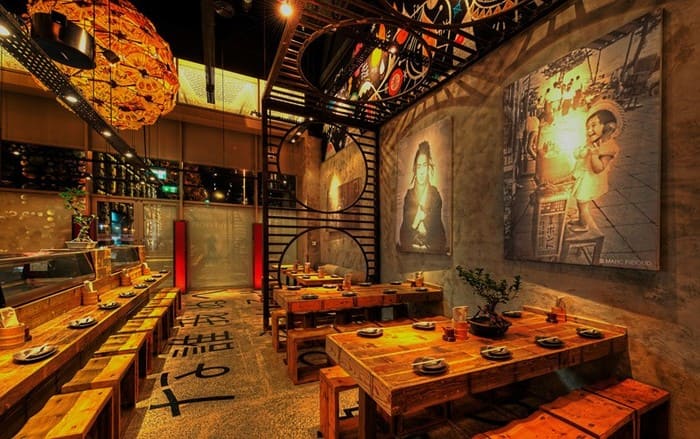 Restaurante japonês estilo rústico, com móveis de madeira, bonsais, e quadros na parede.