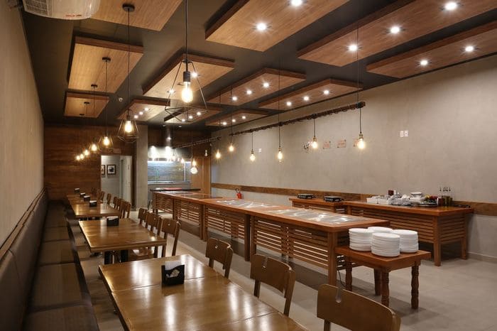 Restaurante Industrial com mesas e cadeiras de madeira, iluminação com pendulos de metal.