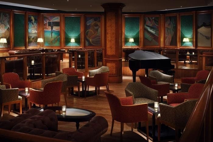 Mesas, poltronas e piano em bar de hotel