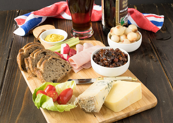 Tábua de cortar carne com salada, queijo, presunto, maçã pão. Cebola em um pote e um copo de cerveja