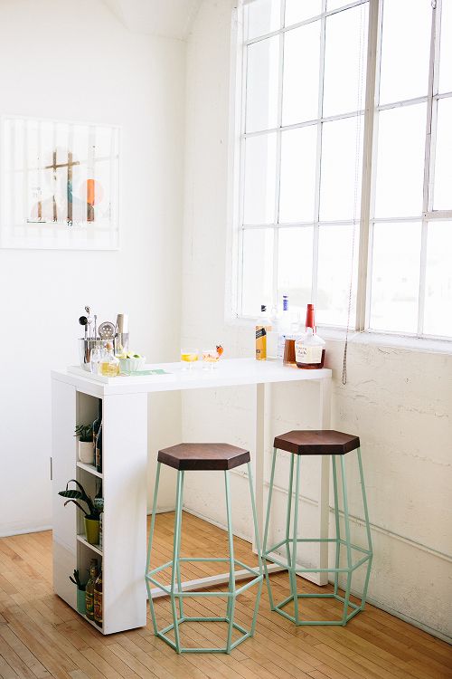 ambiente de cozinha branco com bancada branco próximo a janela com banquetas de design diferenciado na cor verde claro com assento de madeira.