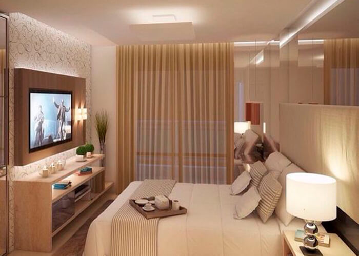 Quarto de casal com decoração nude. Abajur na cabeceira da cama e rack com TV na frente da cama