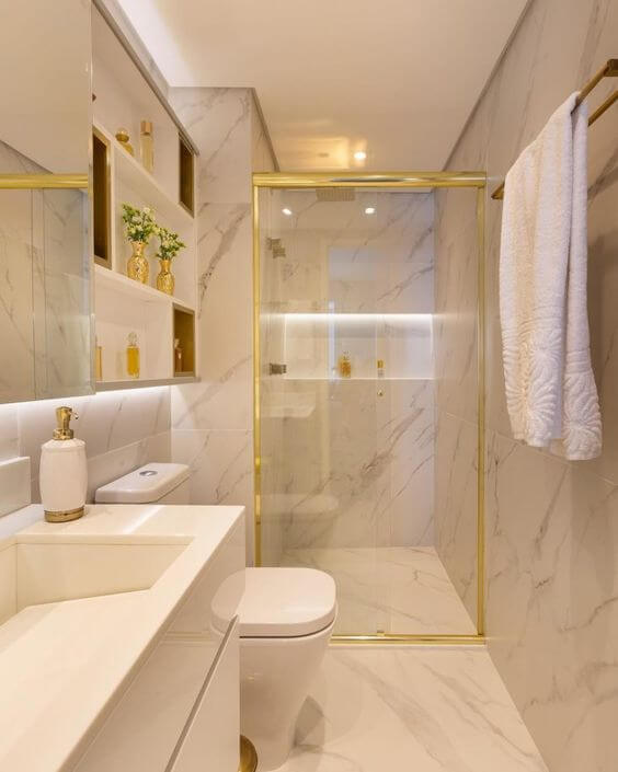 Banheiro com parede e chão com textura de mármore. Box de vidro com estrutura dourada