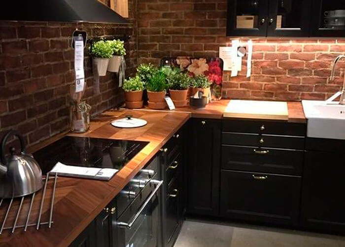 Cozinha preta com madeira, parede de tijolinho, e mini horta em vasinhos de flor