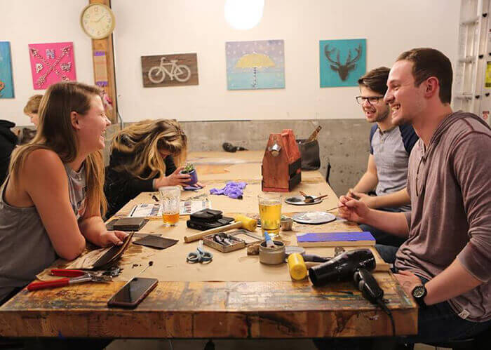 Pessoas sorrindo, sentadas em volta de uma mesa de madeira com várias ferramentas e copos de cerveja