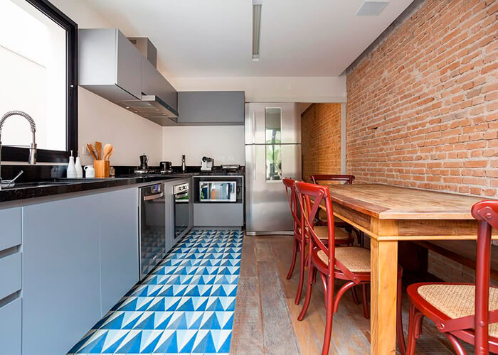 ambiente de cozinha, pia cinza, mesa e cadeiras antigas de madeira, chão metade azulejo outra parte madeira