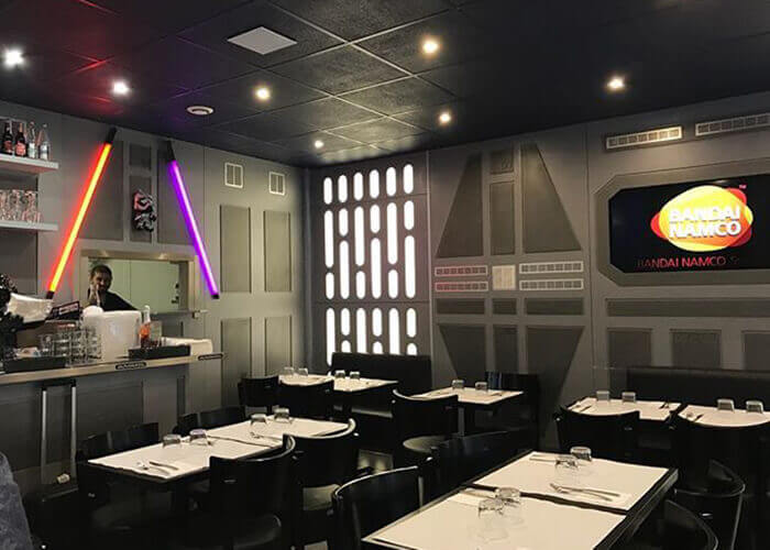 Ambiente temático Star Wars, mesas brancas, cadeiras pretas, parede com textura e decorada com sabre de luz vermelha e roxa