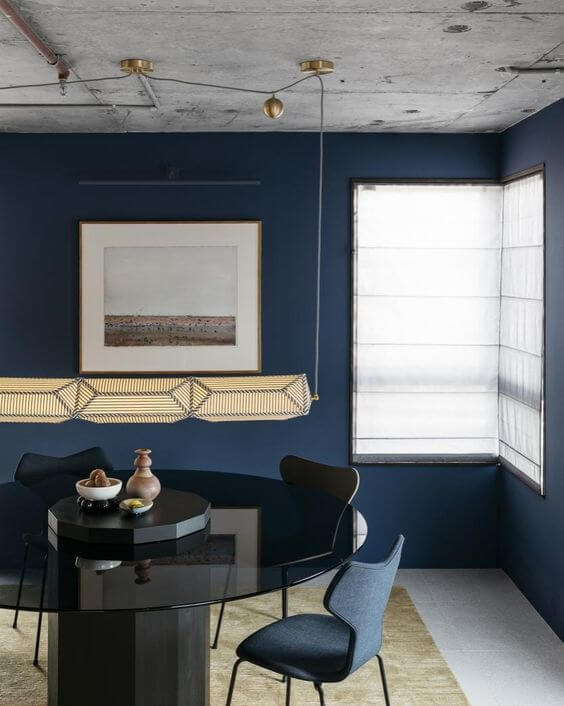 sala de jantar com mesa de vidro, paredes azul marinho e teto cimento queimado