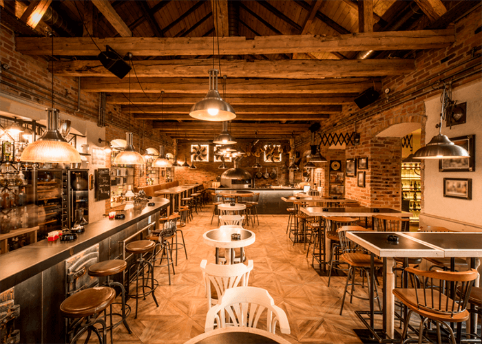 Foto de bar interno com chão de piso que remete tacos de madeiras, banquetas e cadeiras de madeira e ferro. 