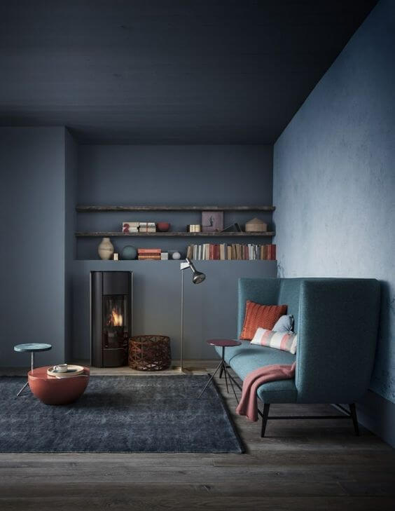 Ambiente com todas as paredes da mesma cor e sofá seguindo o mesmo tom verde acinzentado. Decoração de mesa de centro e almofadas em laranja