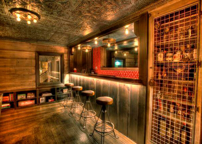 Bar com chão, paredes e balcão em madeira, banquetas de metal com estofado em couro