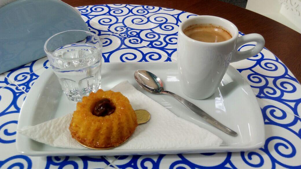 Prato retangular branco com docinho e uma xícara de café. 