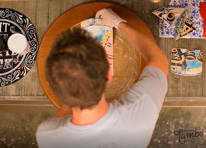 Pessoa colando azulejo em um madeira redonda.