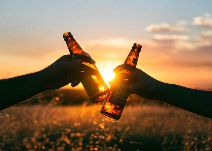 duas-mãos-brindando-com-garrafa-contra-o-sol